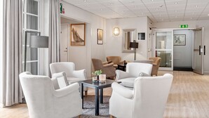 Un moderno vestíbulo de hotel con sofás de cuero blanco, una mesa central con velas y un gran ventanal con cortinas.