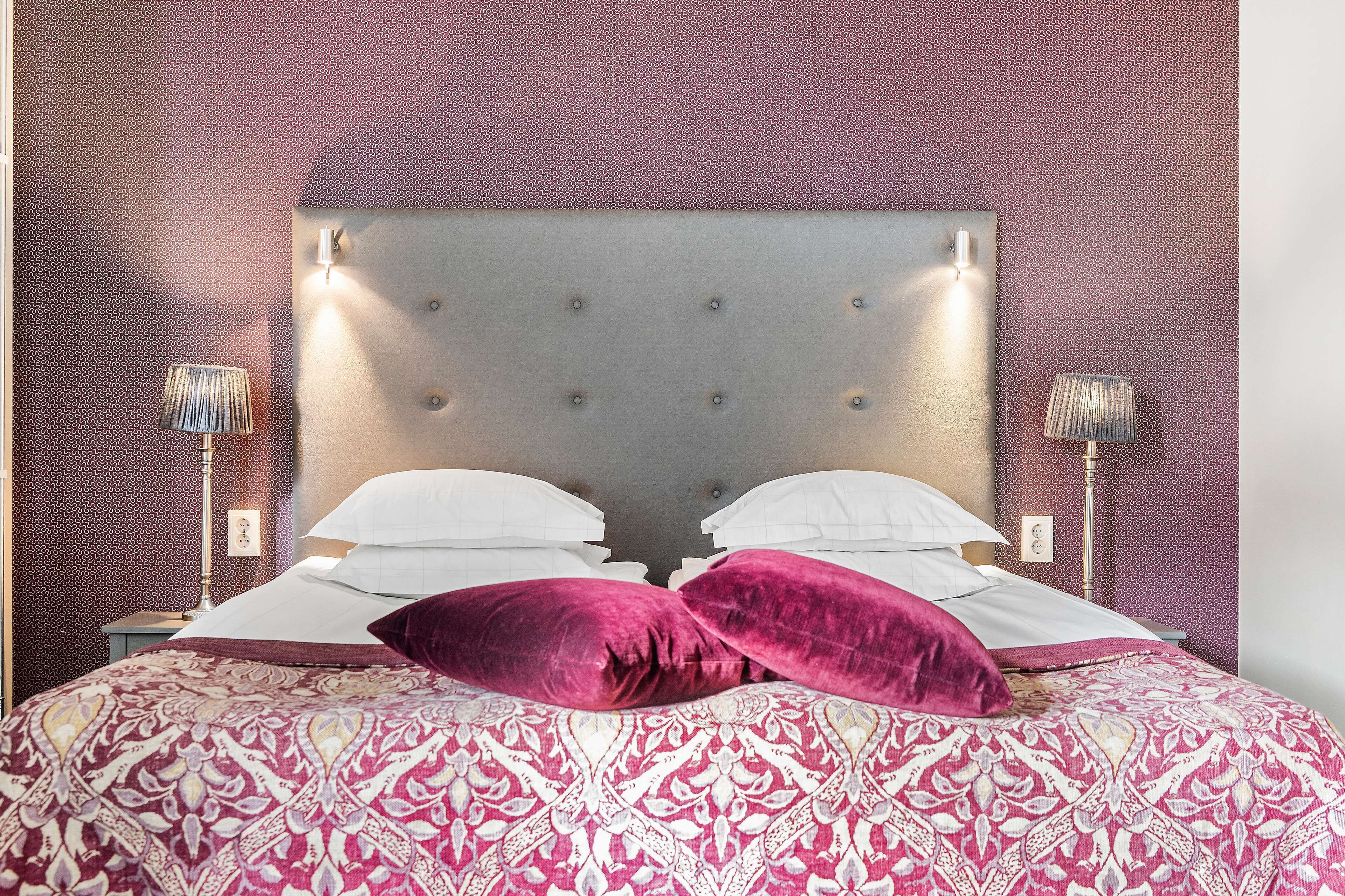 Un lit avec une couvre-lit à motifs, deux oreillers et une tête de lit capitonnée.