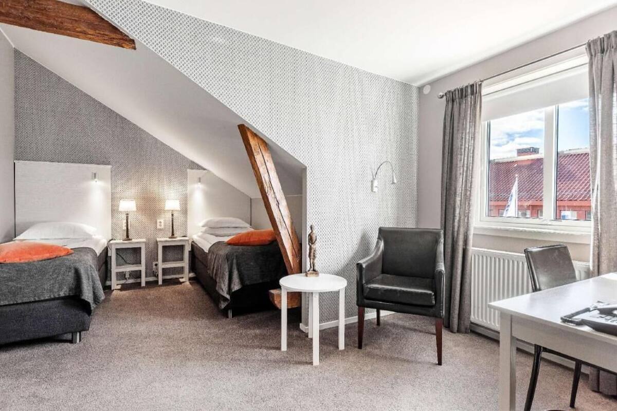 Un dormitorio con dos camas, una mesita, una silla, una ventana con cortinas y un radiador.