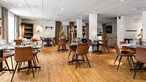 Un comedor amplio con varias mesas y sillas, suelo de madera y un diseño de techo moderno.