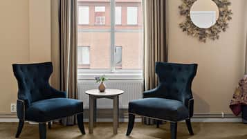 A room with two dark blue armchairs facing each other, a small round table with a vase, and a large mirror on the wall.