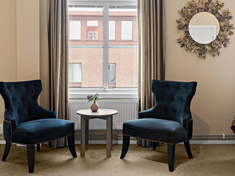 A room with two dark blue armchairs facing each other, a small round table with a vase, and a large mirror on the wall.