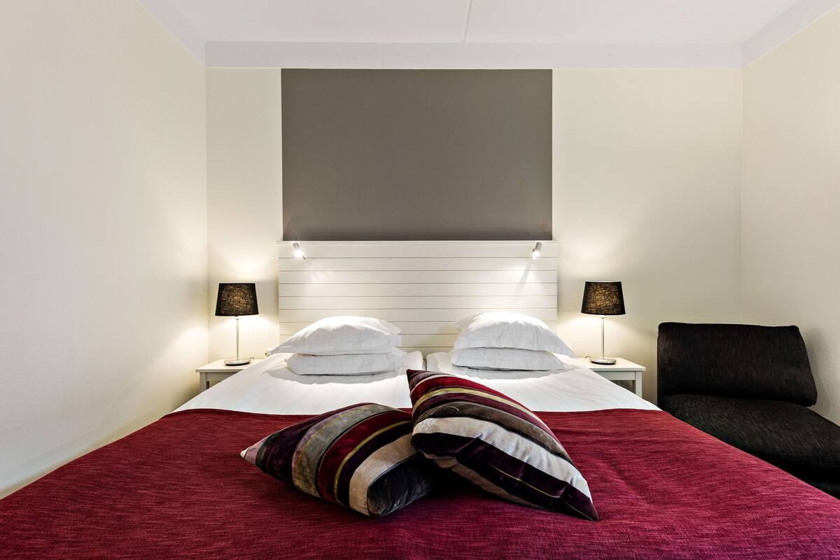 Una habitación de hotel con una cama, dos mesitas de noche, una lámpara y una silla.