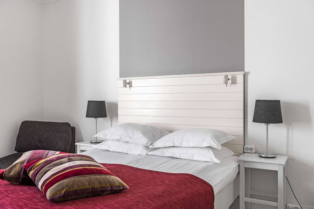 Una habitación de hotel con una cama, dos mesitas de noche, una silla y una manta roja.
