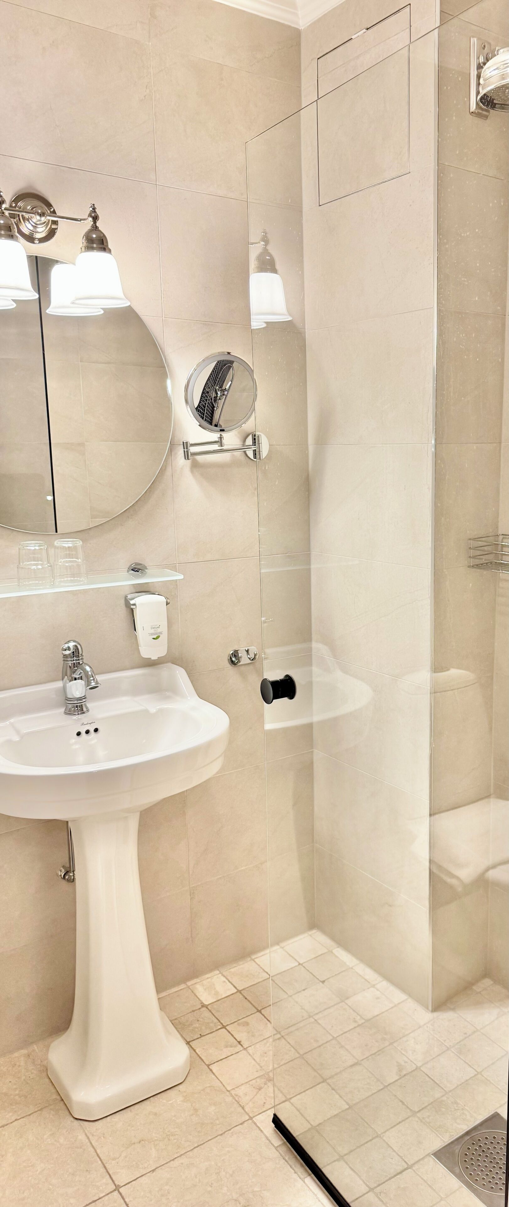 A bathroom with a pedestal sink, a mirror, a glass shower enclosure, and a toilet.