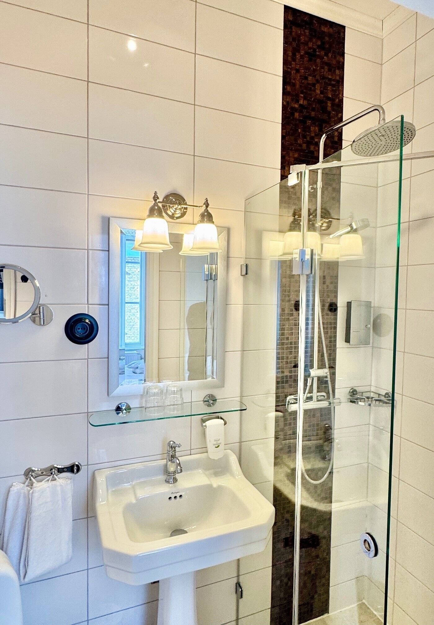 A modern bathroom with a glass-enclosed shower, a white sink, and a mirror with two lights.