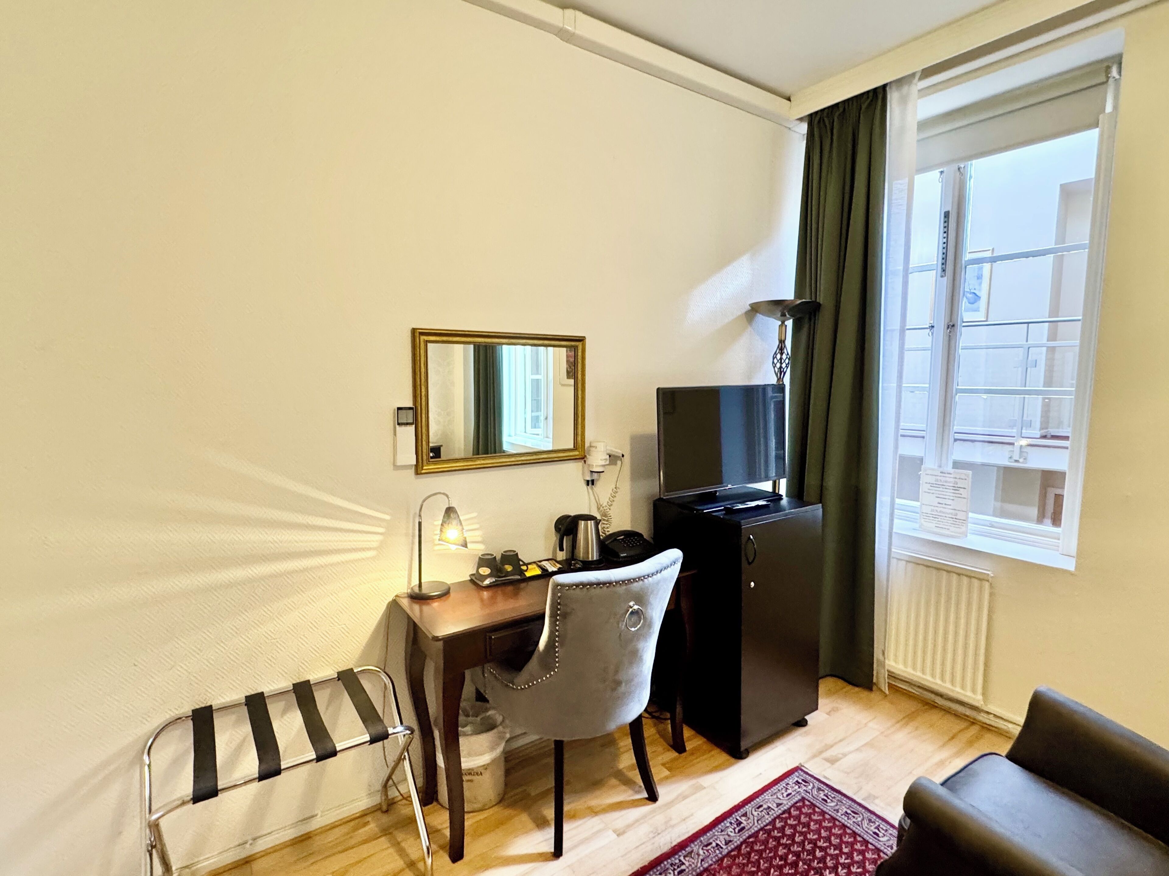 A hotel room with a desk, chair, TV, and a window with curtains.