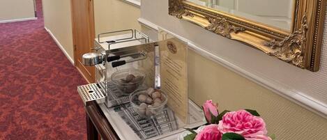 A hallway with a mirror, a coffee machine, and a tray with a flower vase.