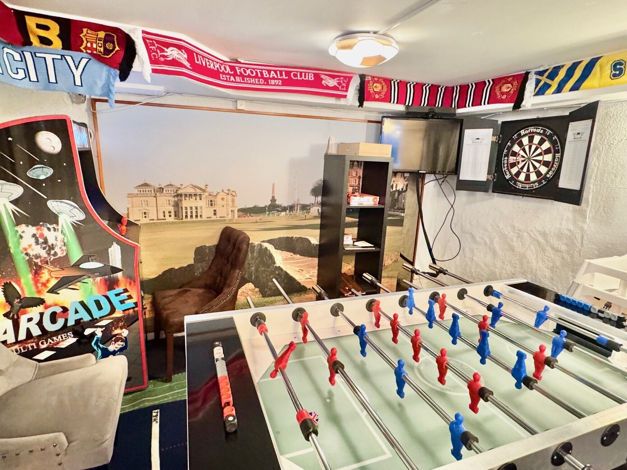 Ein Zimmer mit Kicker, Dartscheibe und einem Poster eines Fußballvereins.
