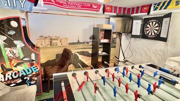 A room with a foosball table, a dartboard, and a poster of a football club.
