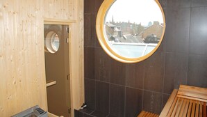 A sauna room with a wooden interior, a round window with a view of buildings, and a bench. - Hotel Concordia (Lund)