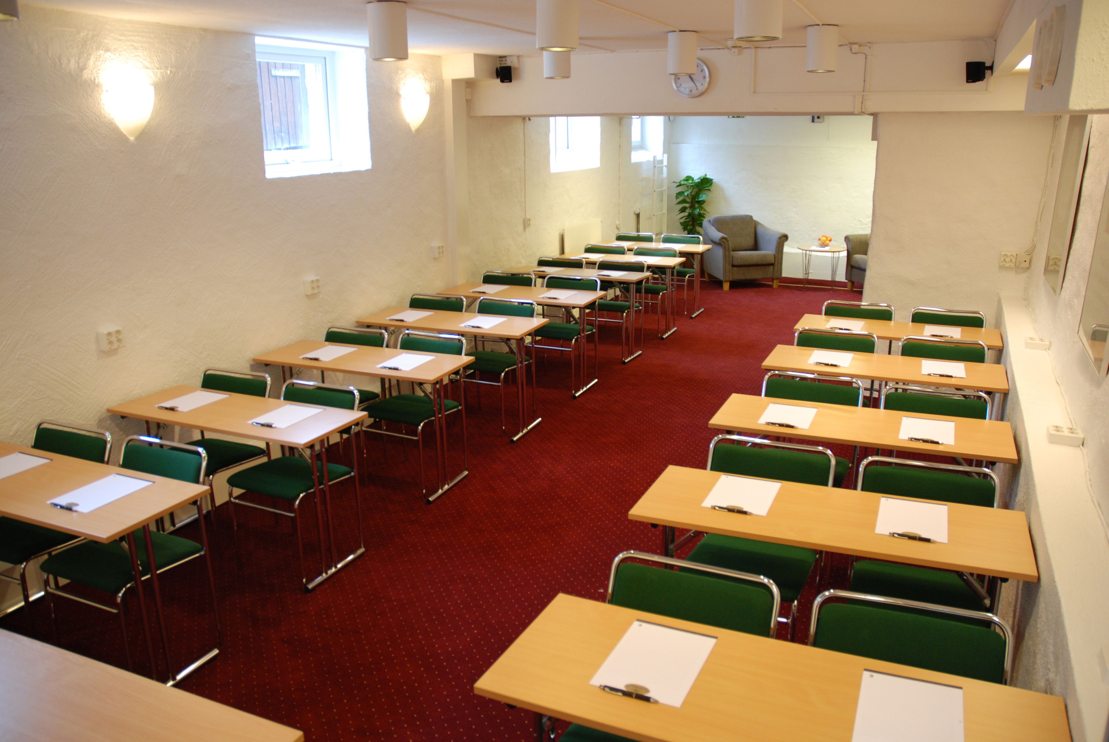 A classroom with rows of desks and chairs, a clock on the wall, and a plant in the corner.