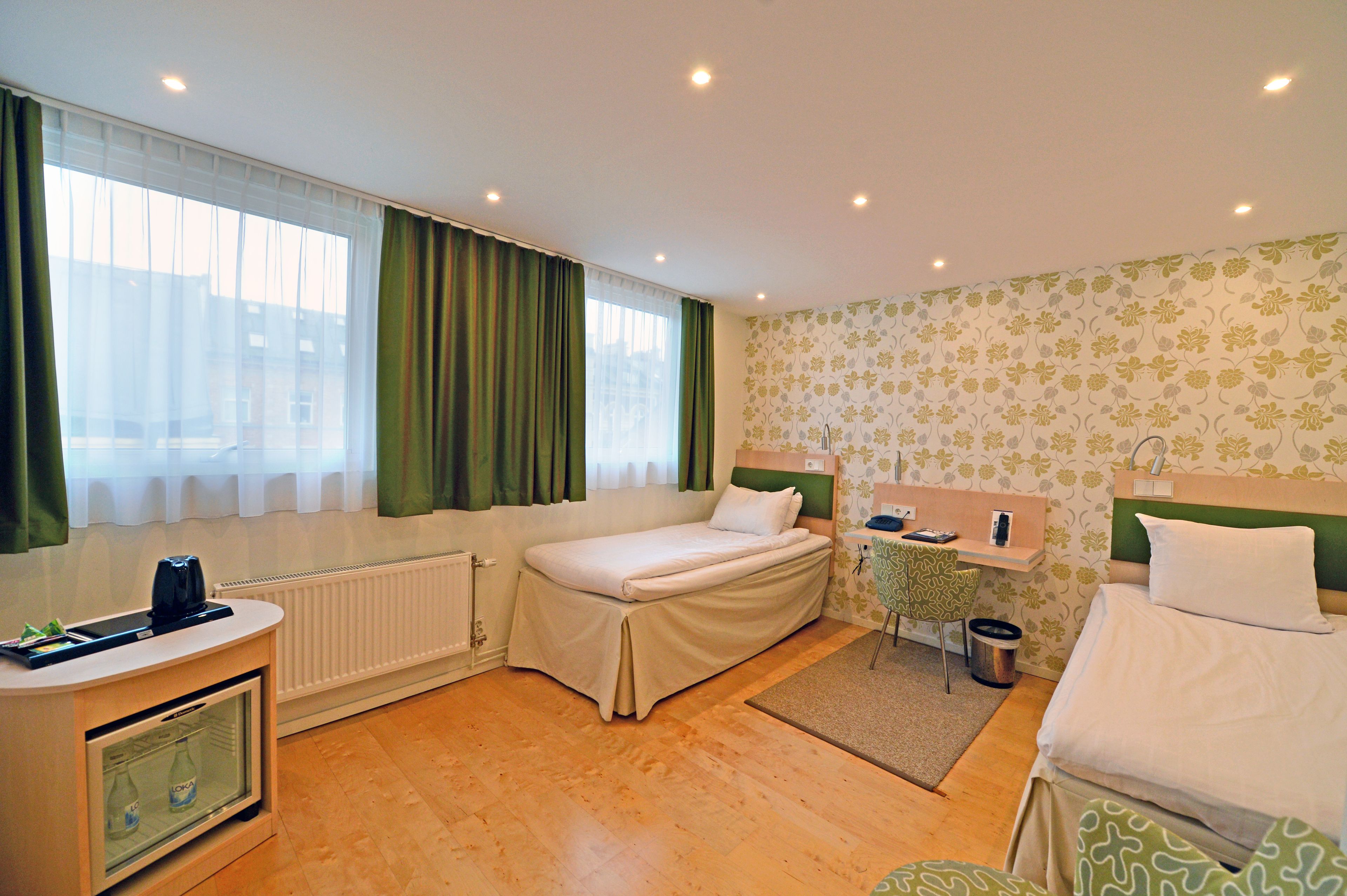 Hotelkamer met een bed, bureau, stoel, radiator en raam met gordijnen.