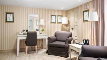 A hotel room with striped wallpaper, a desk with a chair, a sofa, and two lamps.