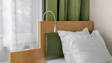 A hotel room with a wooden headboard, a green upholstered headrest, white bedding, and a window with sheer curtains.