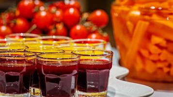 A tray of glasses filled with a red beverage, a large carved pumpkin, and a bunch of red tomatoes in the background.