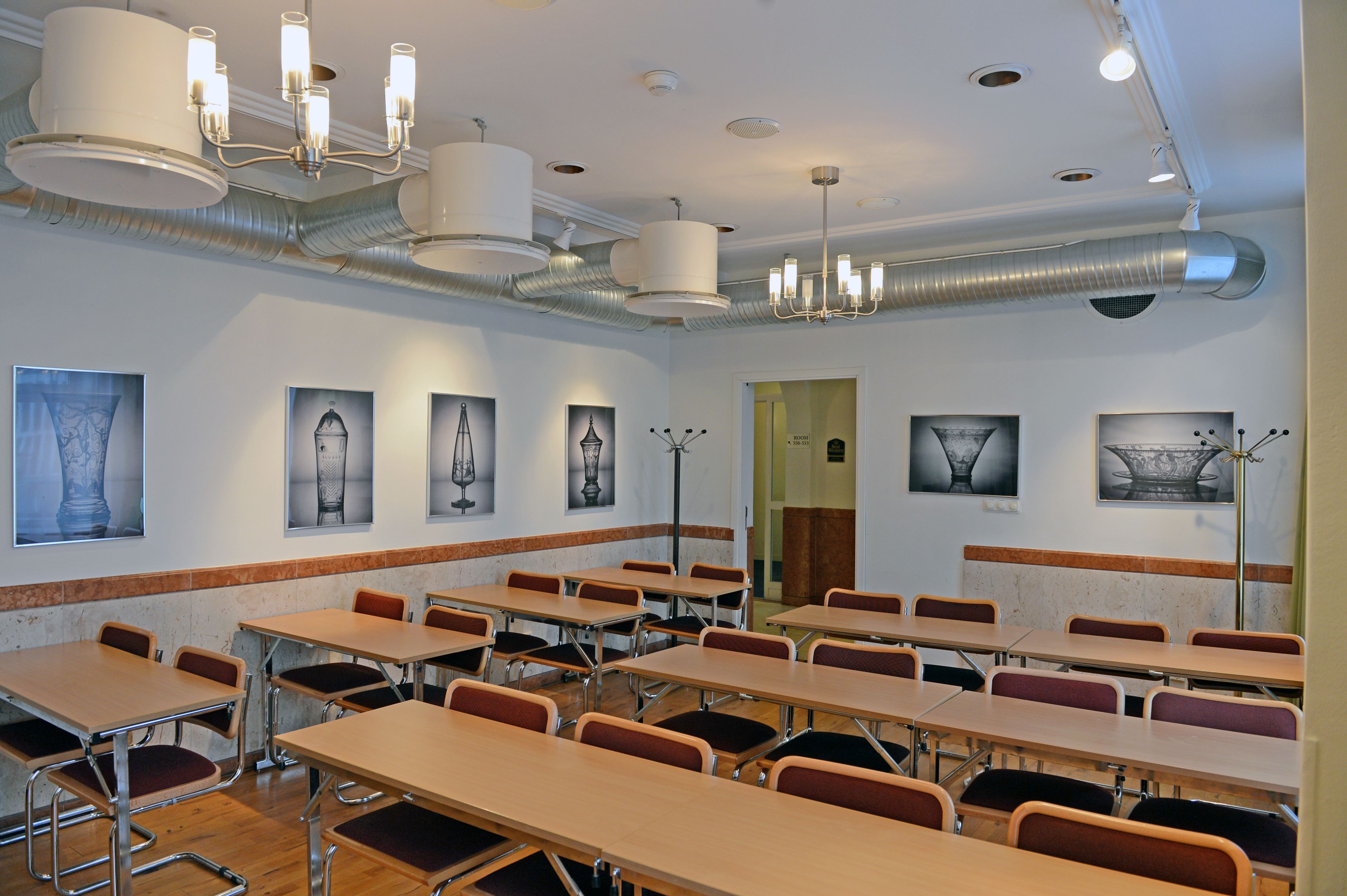 A conference room with tables and chairs, a chandelier, and artwork on the walls.