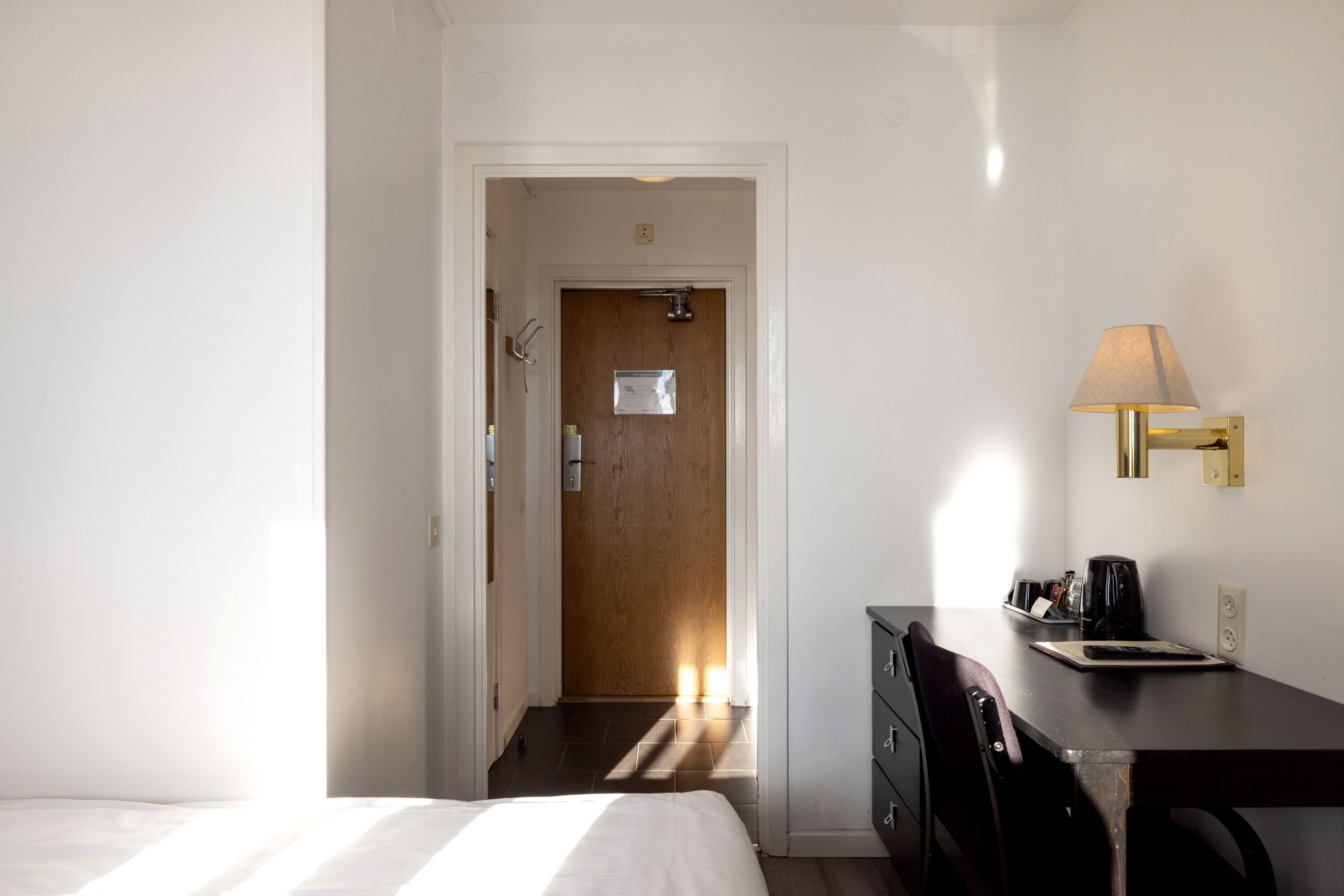 Una habitació d'hotel amb un llit, un escriptori amb una làmpada i una porta que dona a una altra habitació.