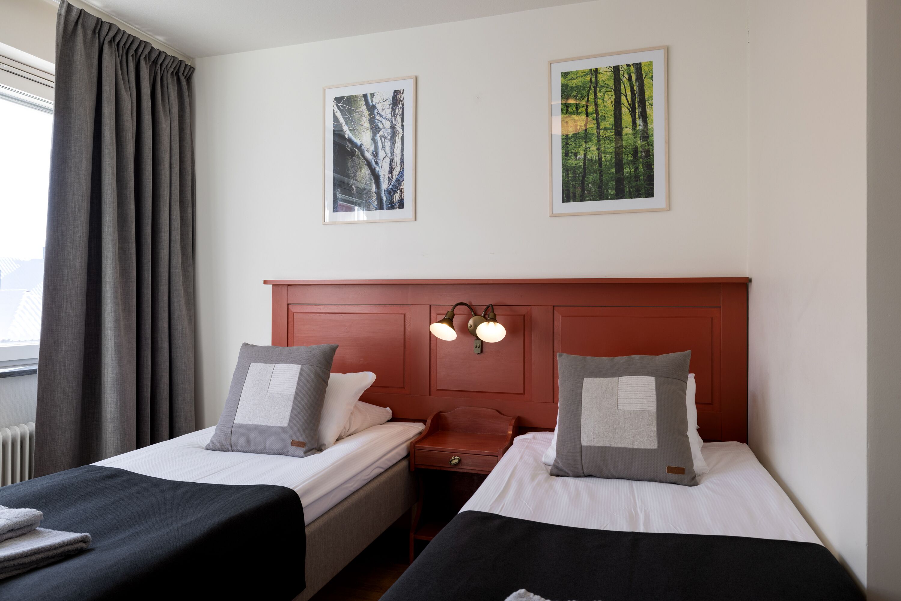 A hotel room with two beds, a nightstand, a red headboard, and two framed pictures on the wall.