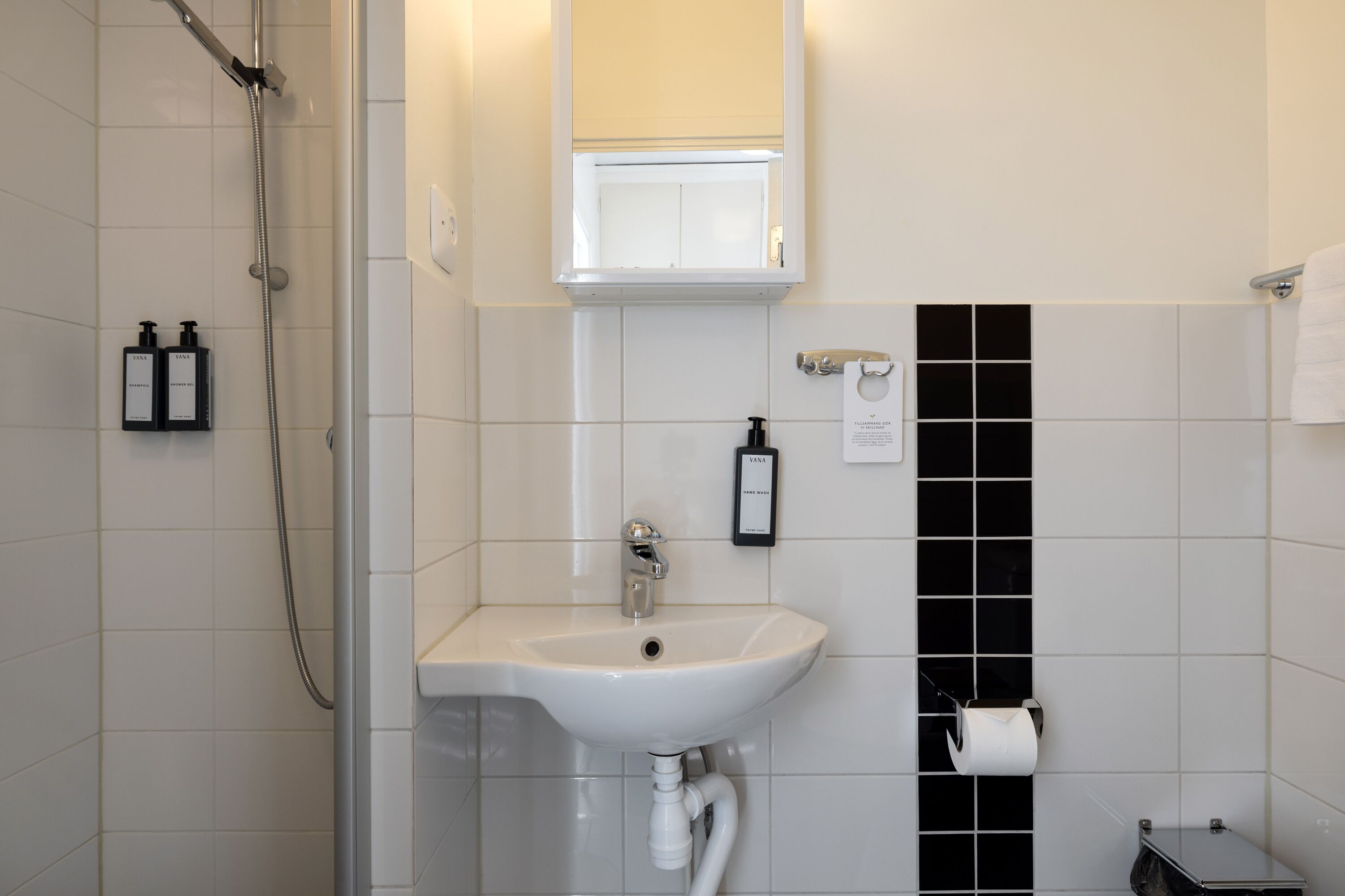 Ein Badezimmer mit einem weißen Waschbecken, einem Spiegel und einer schwarzen Wand mit Fliesen.