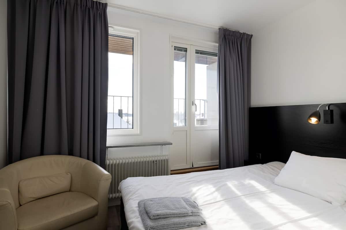 A hotel room with a bed, a chair, and a view of the city through the window.
