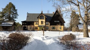 A large, traditional wooden house with a steeply pitched roof, surrounded by snow-covered ground and sparse vegetation. - Hotel Bishops Arms Mora (Mora)