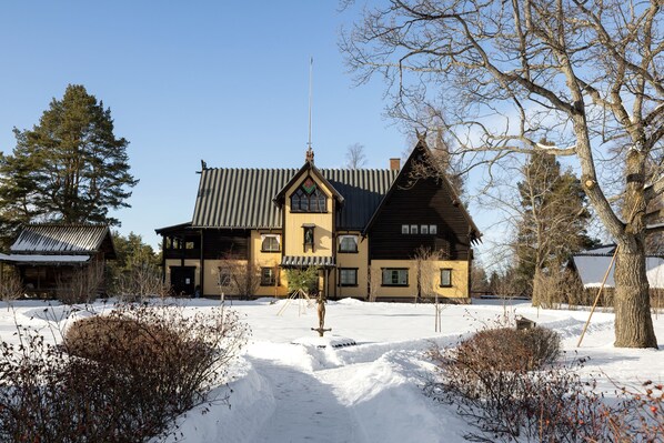 A large, traditional wooden house with a steeply pitched roof, surrounded by snow-covered ground and sparse vegetation. - Hotel Bishops Arms Mora (Mora)