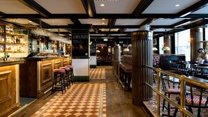 A bar area with a checkered floor, wooden bar counter, stools, and a menu board. - Hotel Bishops Arms Mora (Mora)