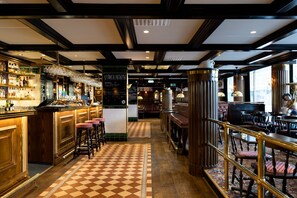 Uma área de bar com piso xadrez, balcão de madeira, banquetas e um quadro de cardápio.