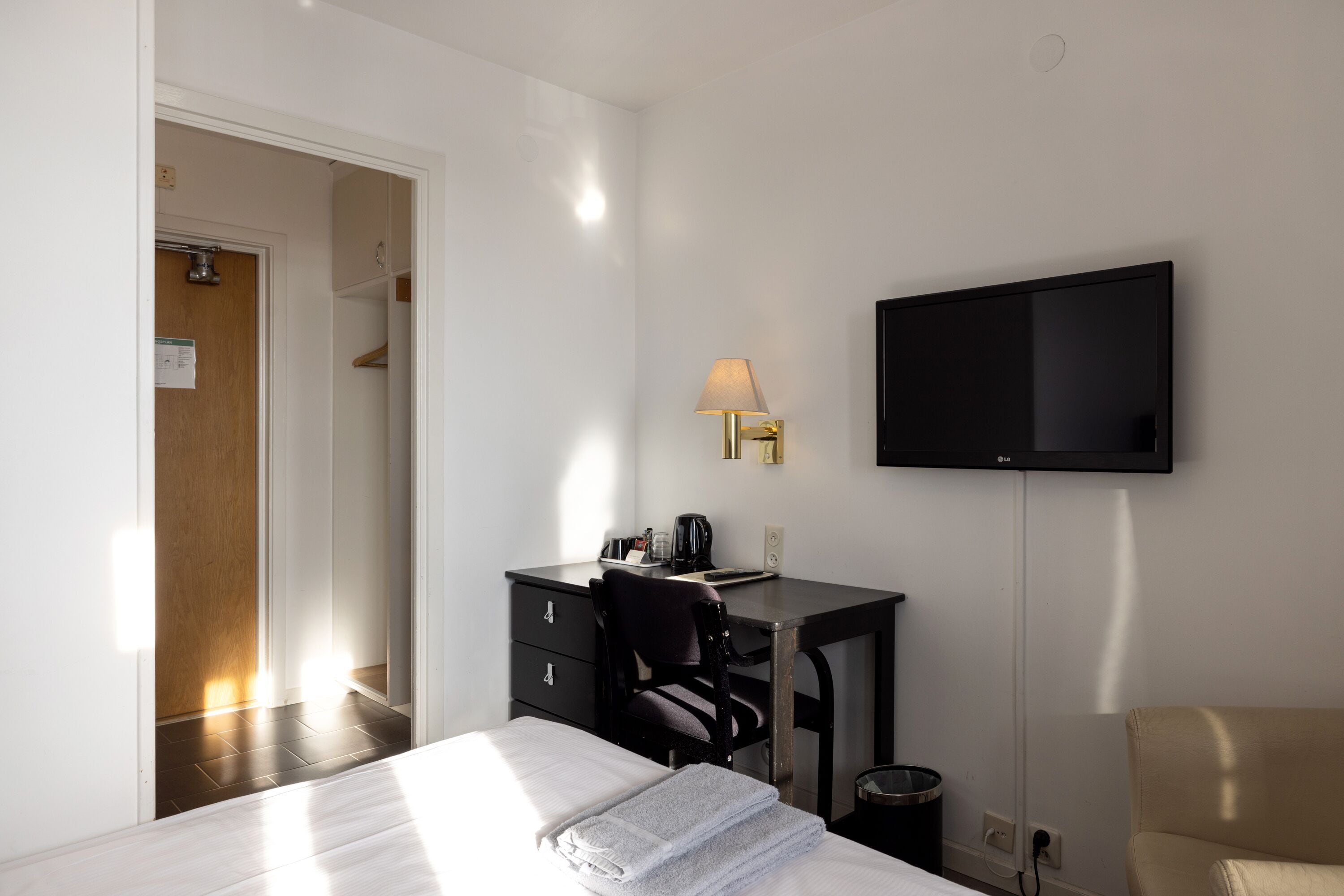 A hotel room with a bed, a desk, a chair, a television, and a lamp.