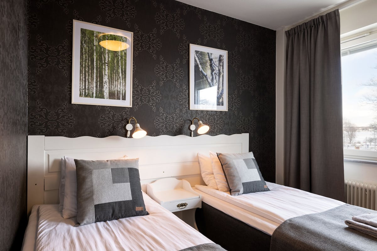 A hotel room with two beds, a white headboard, and two framed pictures on the wall.