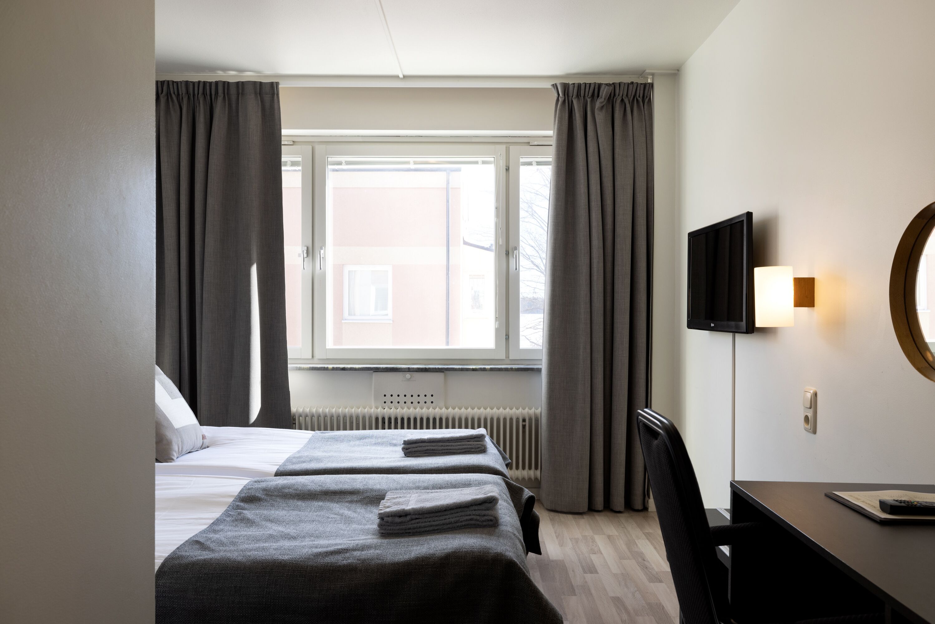 Une chambre d’hôtel avec deux lits, un bureau, une chaise, une télévision et une fenêtre avec des rideaux.