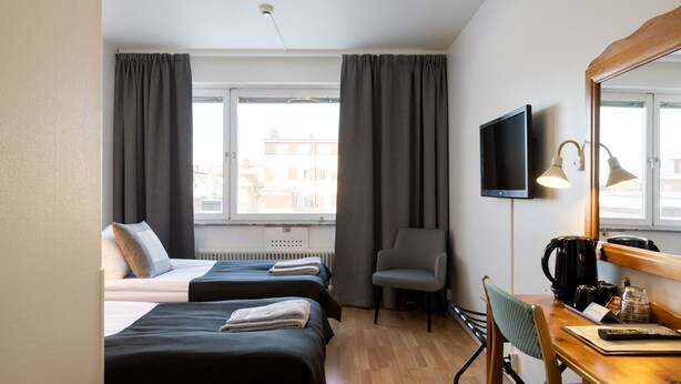 A hotel room with two beds, a desk with a chair, a television, and a window with curtains. - Hotel Bishops Arms Mora (Mora)