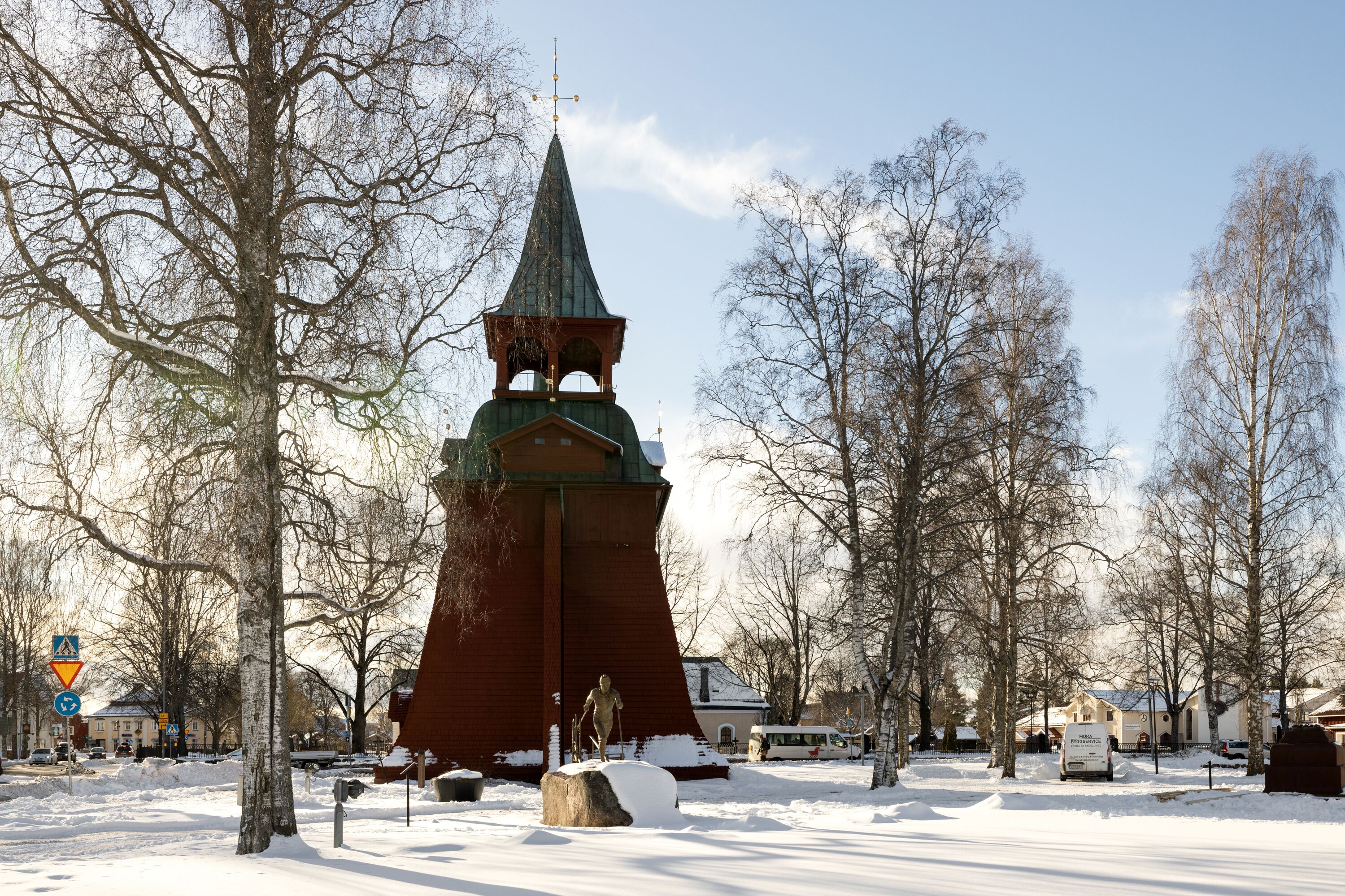 Una iglesia cubierta de nieve con un campanario alto, rodeada de árboles desnudos y un cielo despejado.