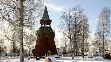 Una iglesia cubierta de nieve con un campanario alto, rodeada de árboles desnudos y un cielo despejado.