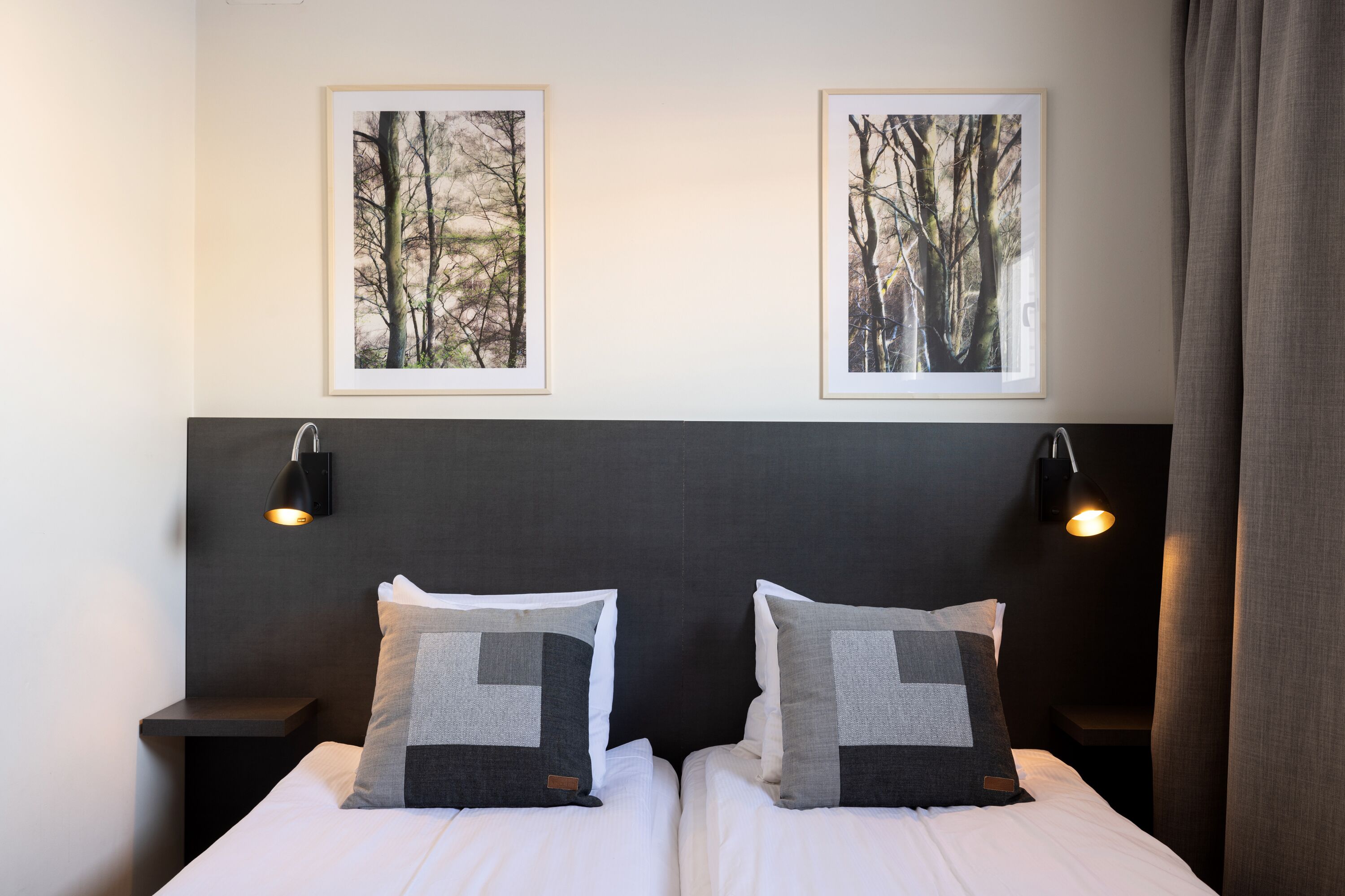 A double bed with two pillows, a headboard, and two wall-mounted lamps.