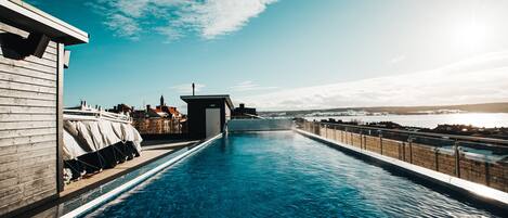 A long, narrow swimming pool with a clear blue water surface, surrounded by a wooden deck and a metal railing.