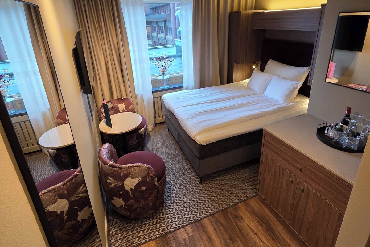 A hotel room with a bed, bedside table, mirror, and a view of the outside.