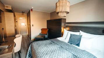 Une chambre d’hôtel moderne avec un grand lit, une table de chevet, une chaise et un luminaire suspendu.