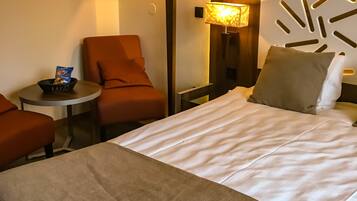 A hotel room with a bed, two armchairs, a small table with snacks, and two lamps.