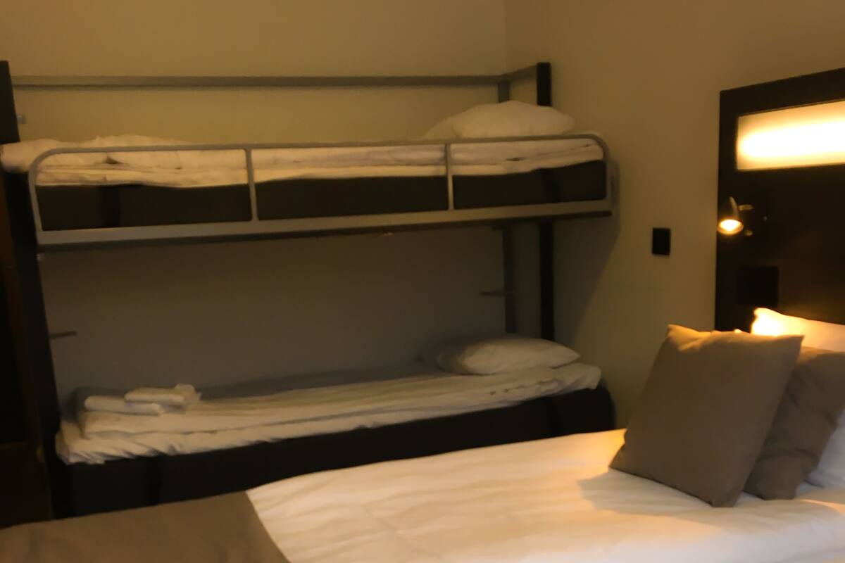 A bunk bed with white bedding and a wooden table in front.