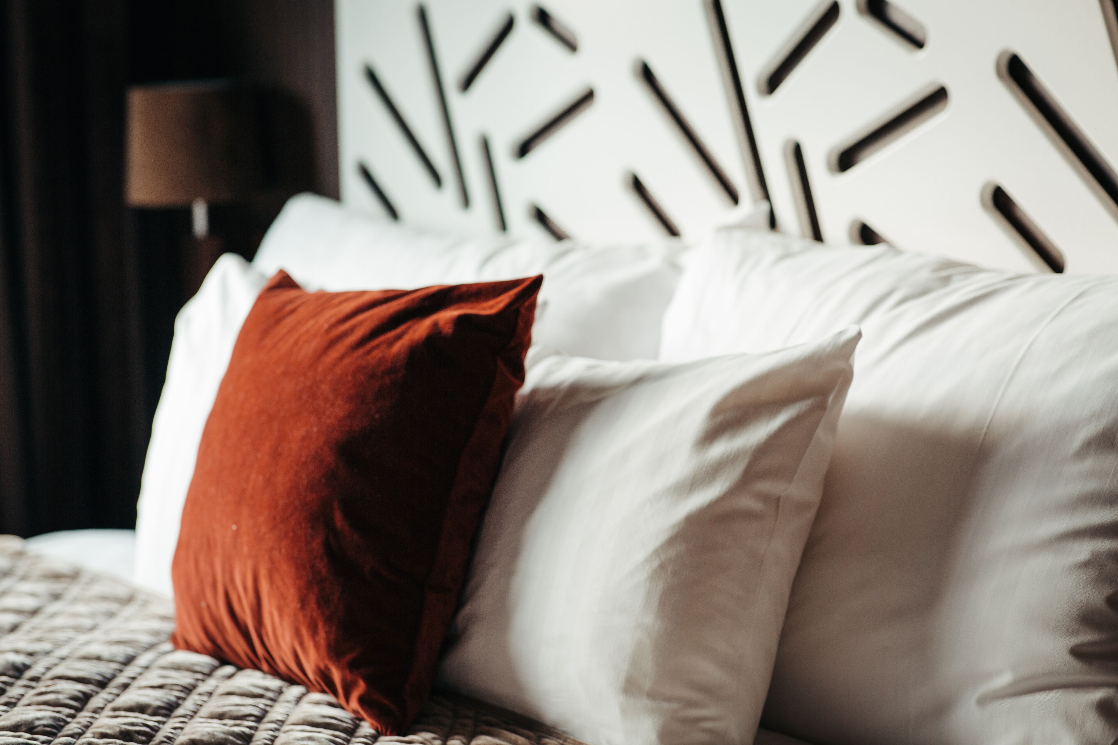 A bed with white and brown pillows, a textured blanket, and a modern headboard with geometric patterns.