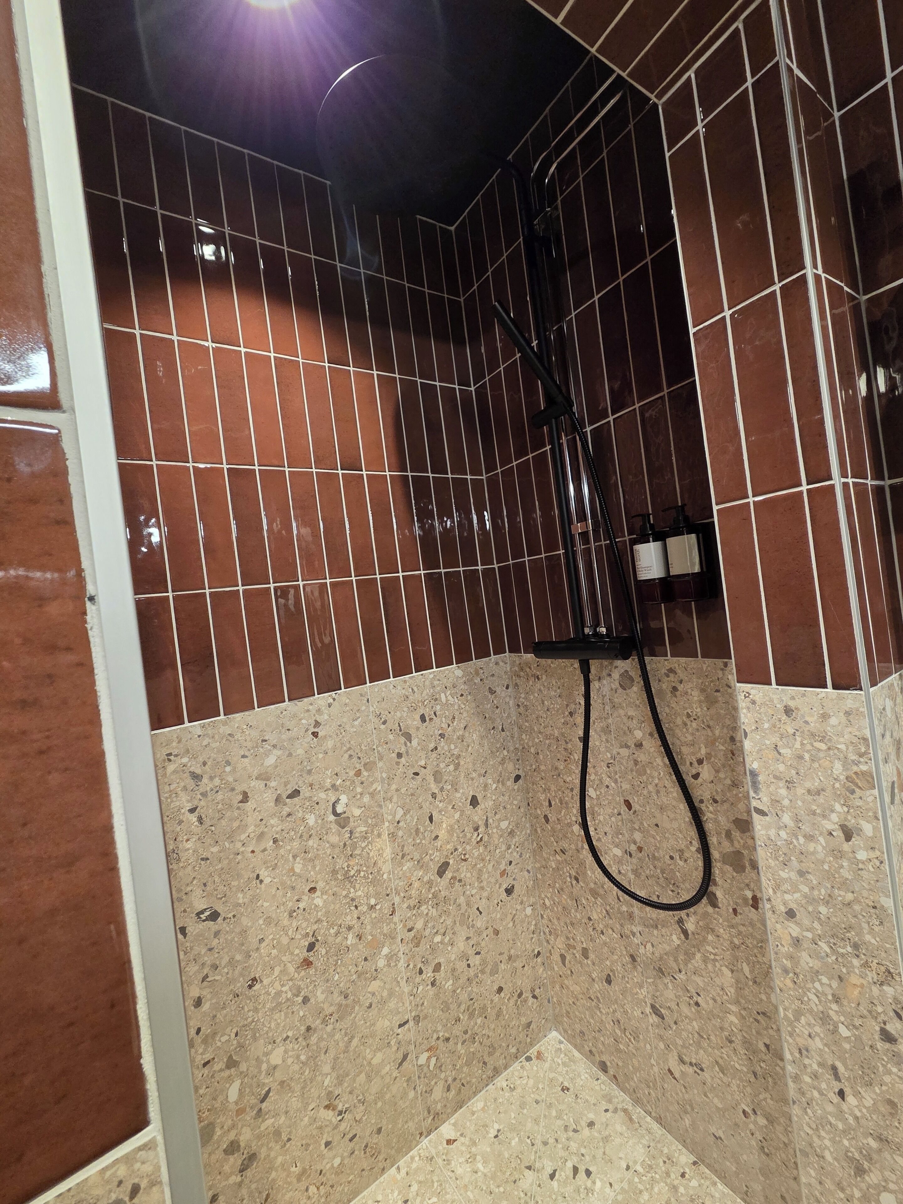 A bathroom with tiled walls, a shower area, and a hand dryer.