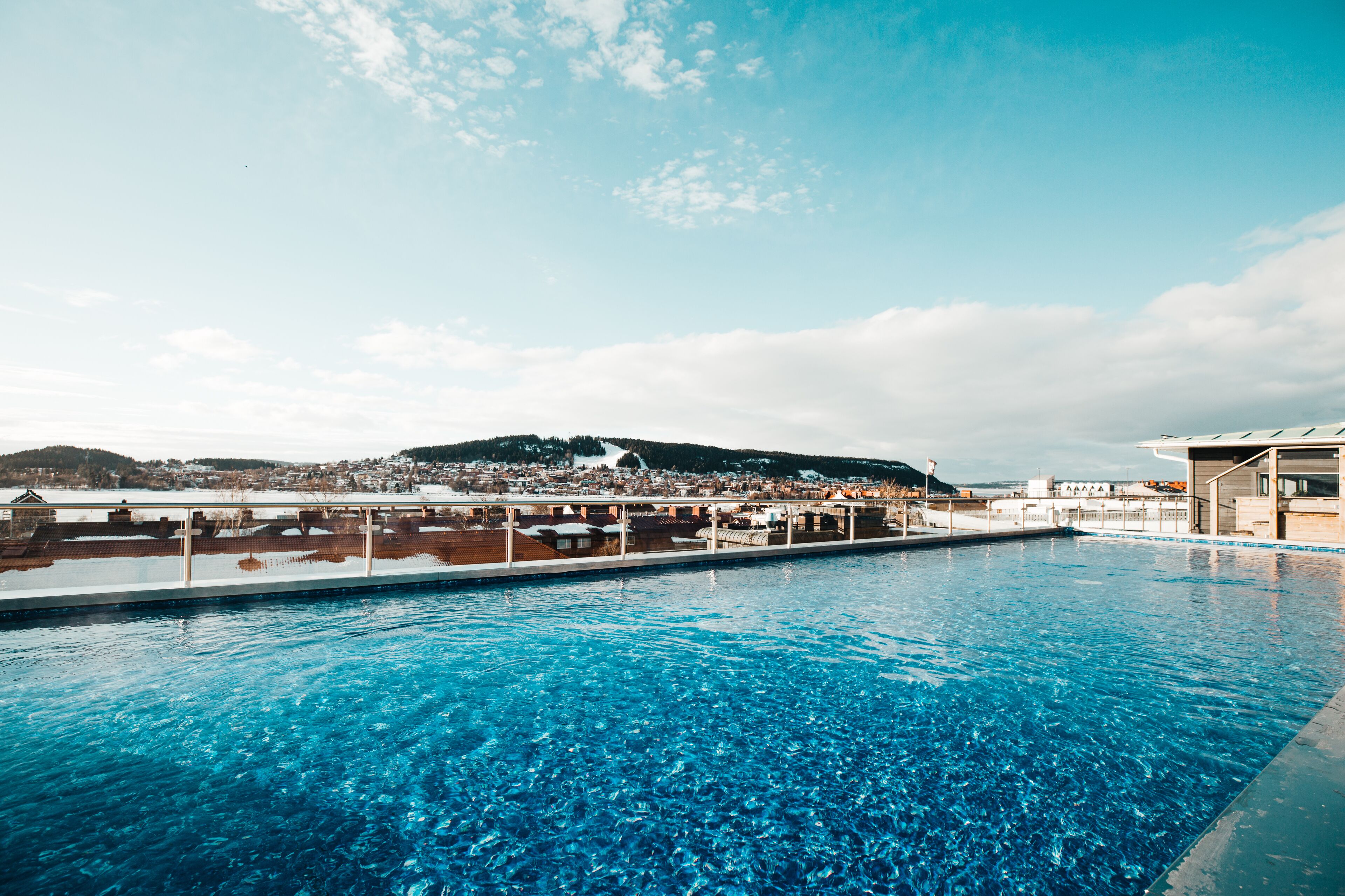 Una piscina con agua azul cristalina, rodeada de edificios y una colina distante.