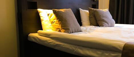 Habitación de hotel con cama, almohadas y cabecera con iluminación integrada.