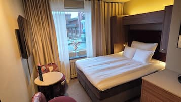 Habitación de hotel con cama, escritorio, silla, ventana con cortinas e iluminación en el techo.