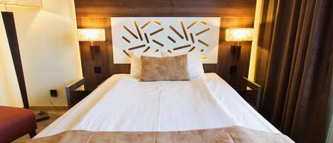 A hotel room with a large bed, two bedside lamps, a wooden headboard, and a red bench.
