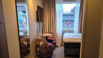 Une chambre d’hôtel équipée d’un lit, d’un bureau, d’une chaise, d’un canapé, d’un miroir et d’une fenêtre avec des rideaux.