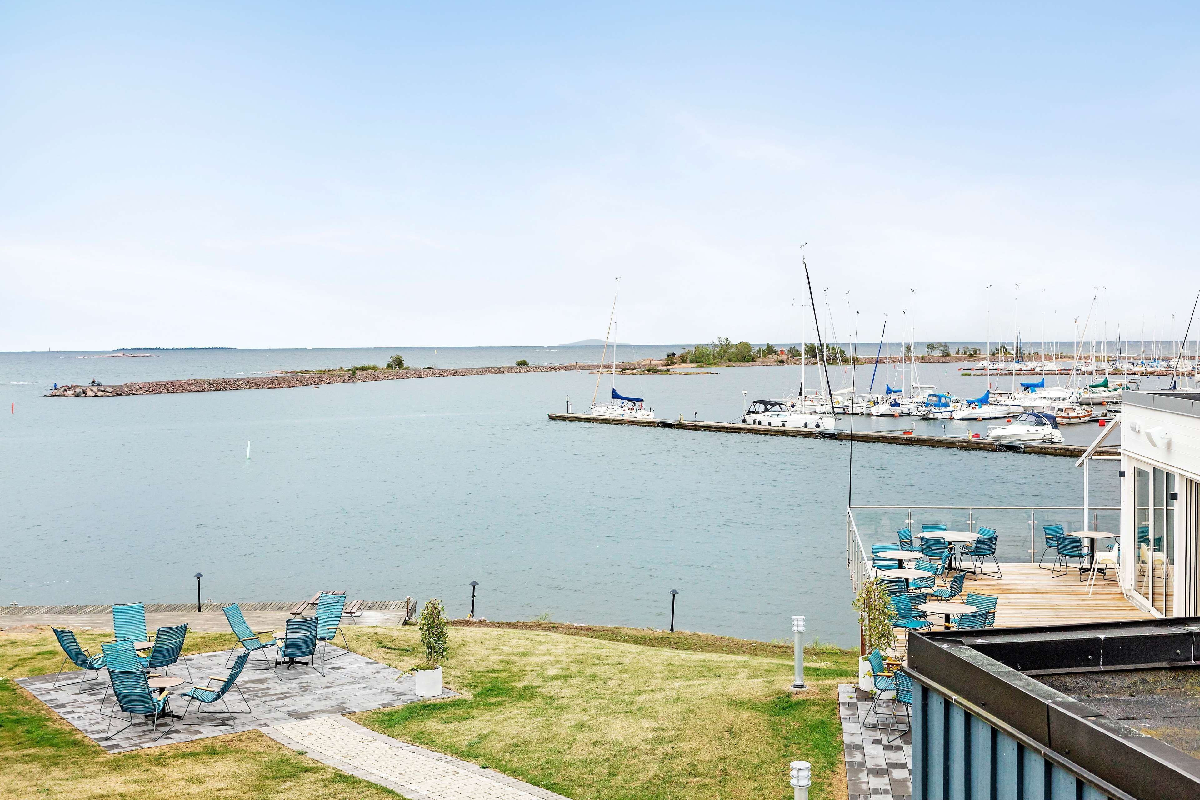 A marina with boats docked, a grassy area with outdoor seating, and a building with a balcony overlooking the water.