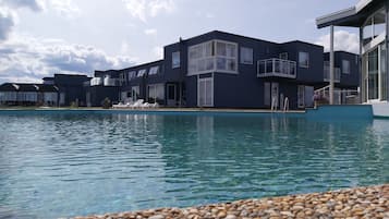 Un bâtiment moderne doté d’une piscine, de chaises longues et d’une plage de galets.
